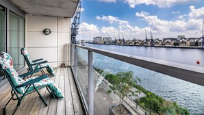 Un balcon avec deux fauteuils de jardin, une vue sur une rivière et un paysage urbain en arrière-plan.