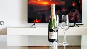 Une bouteille de vin Cava Brut et deux verres sur une table, dans un intérieur moderne, avec une peinture représentant un coucher de soleil en arrière-plan.
