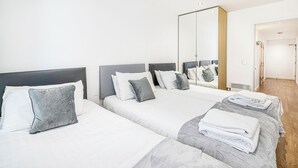 Une chambre d’hôtel avec deux lits, une literie grise et blanche, un grand miroir et un plancher en bois.