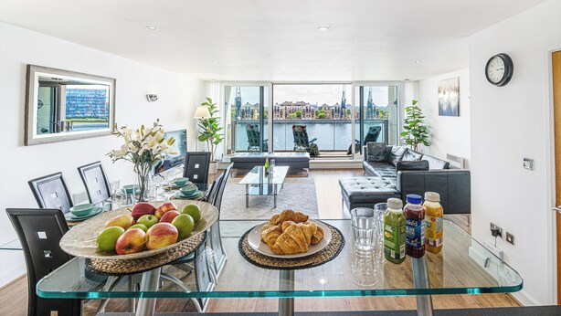 Un salon moderne avec une table à manger en verre, un canapé et une vue sur une rivière et des immeubles.