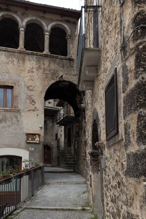A narrow alleyway with stone buildings, a metal gate, and a staircase leading to an upper level.