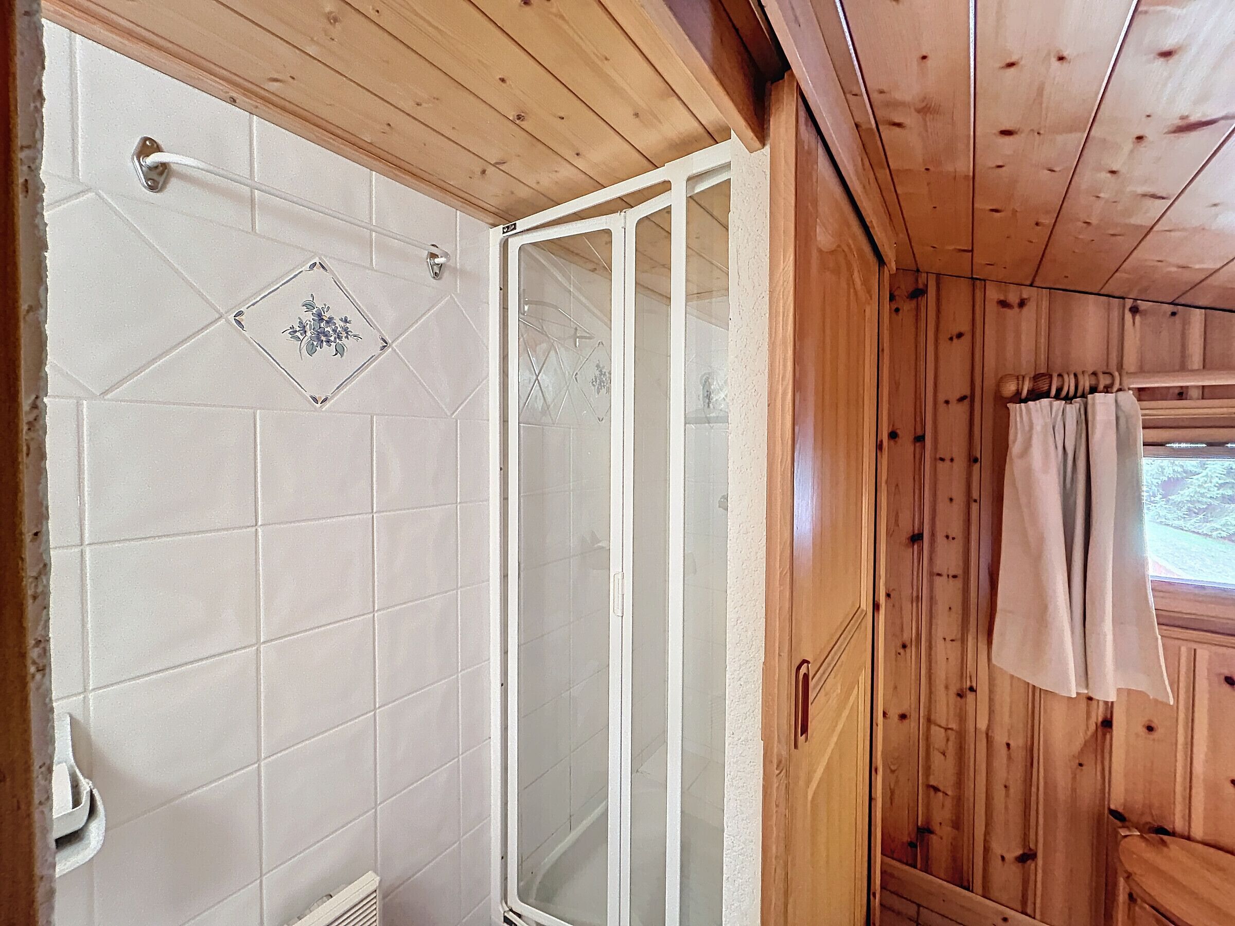 A wooden cabin with a shower area featuring white tiles and a glass door.