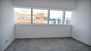 Um quarto com uma janela grande, paredes lisas e chão de azulejos.