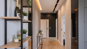 A modern hallway with wooden flooring, built-in shelves with plants and books, a small table with a candle, and a door leading to another room. - Lumina Apart near Pasaż Łódzki (Łódź)