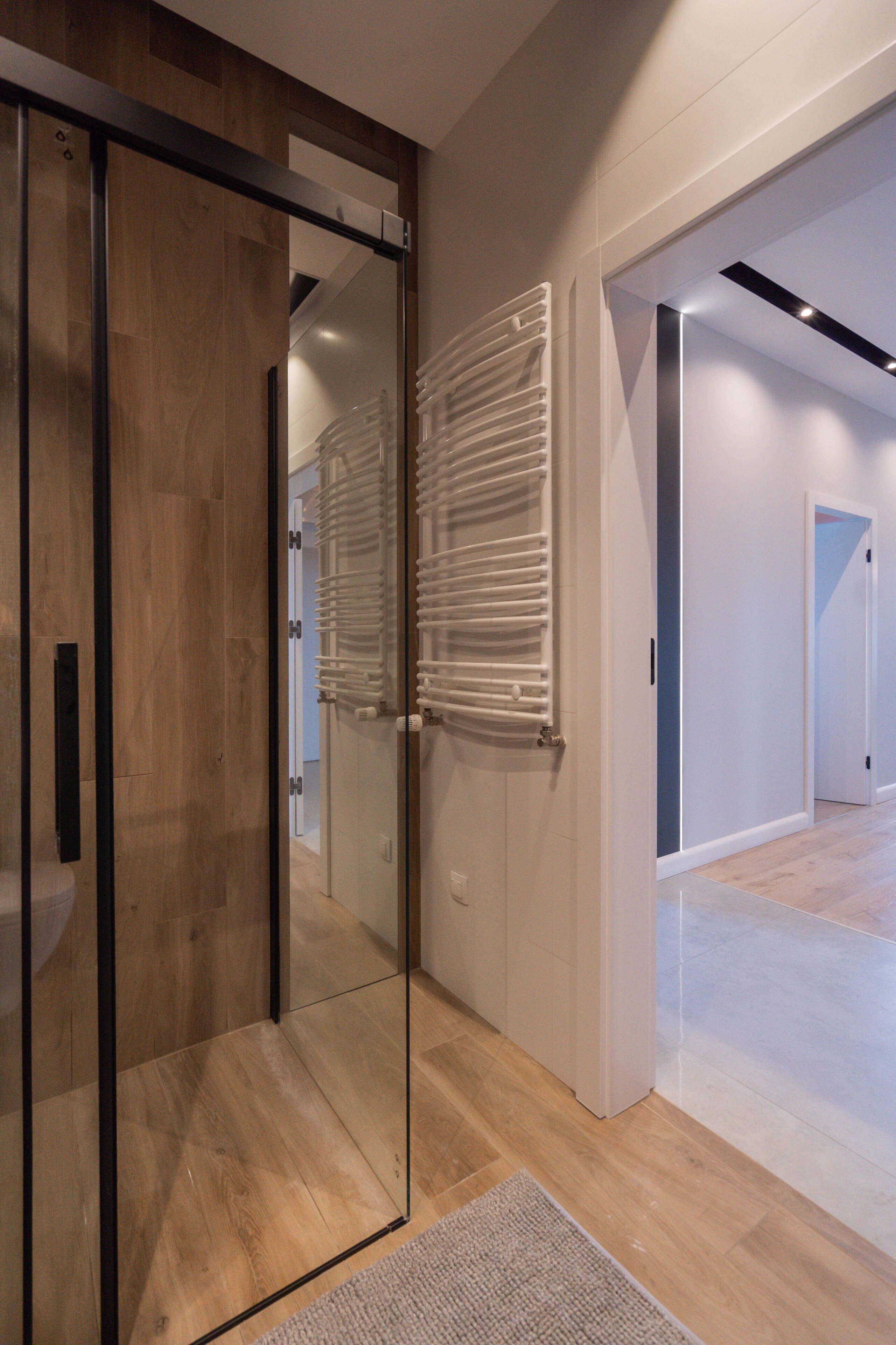 A modern hallway with a glass door, a white radiator, and a wooden floor.