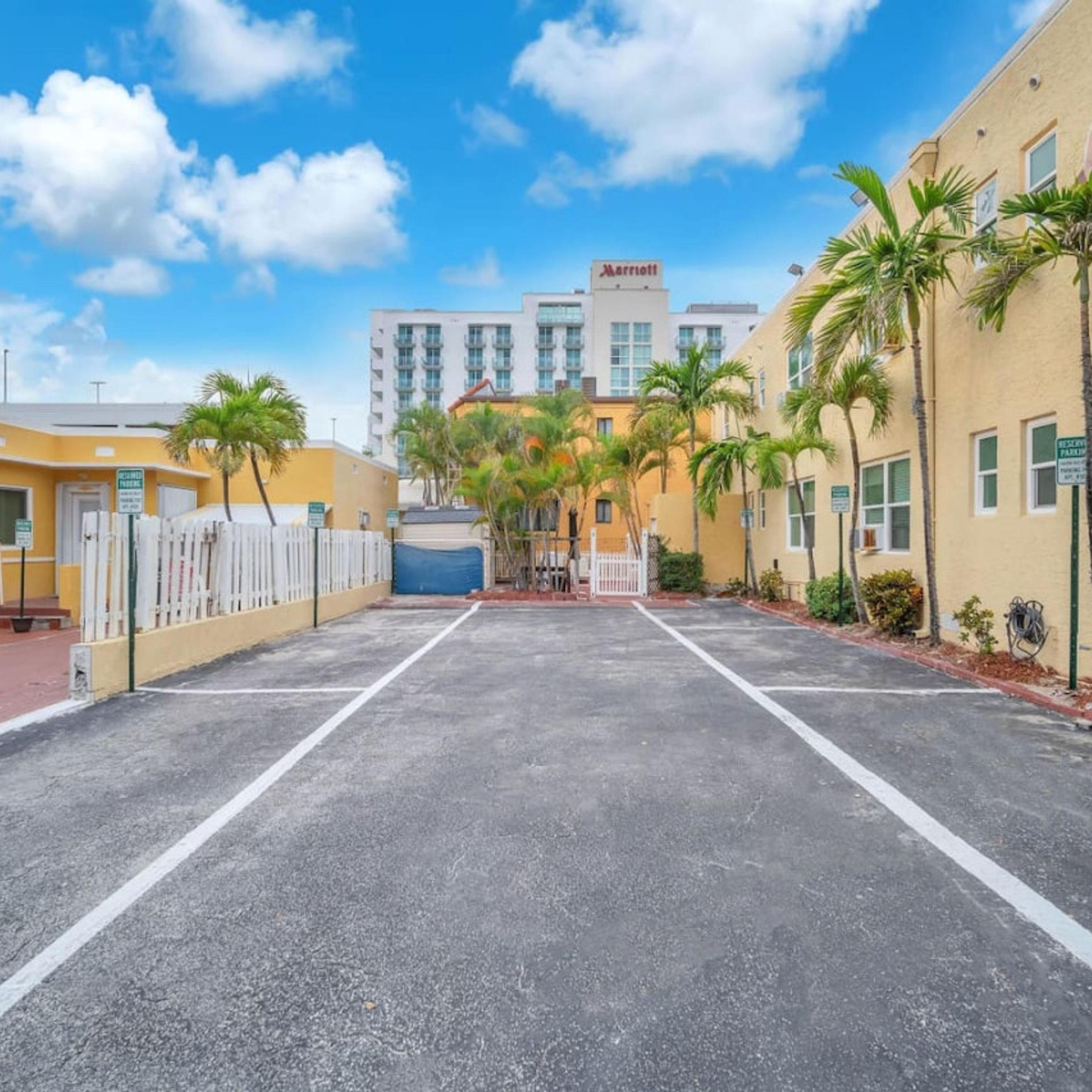 A Marriott hotel with a parking lot, palm trees, and a clear blue sky.