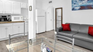 A modern living room with a glass coffee table, a gray sofa with red cushions, and a kitchen in the background. - American Dream Just Steps to the Beach (Hollywood)