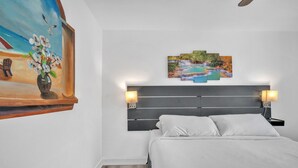 Ein Schlafzimmer mit einem Bett, einem Kopfteil, Nachttischlampen, einem Gemälde und drei Landschaftsbildern über dem Bett.