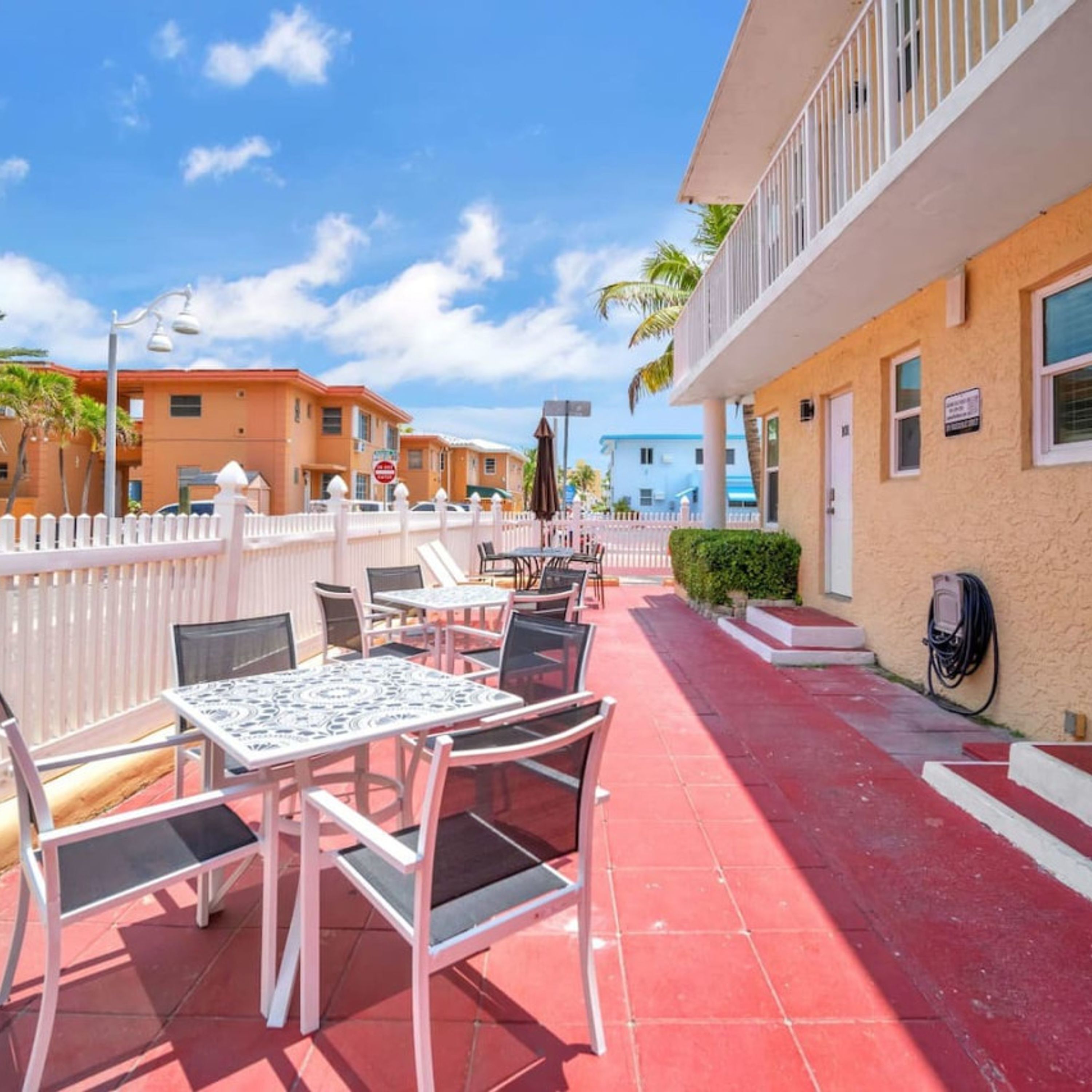 An outdoor patio with tables and chairs, a white fence, and buildings in the background.