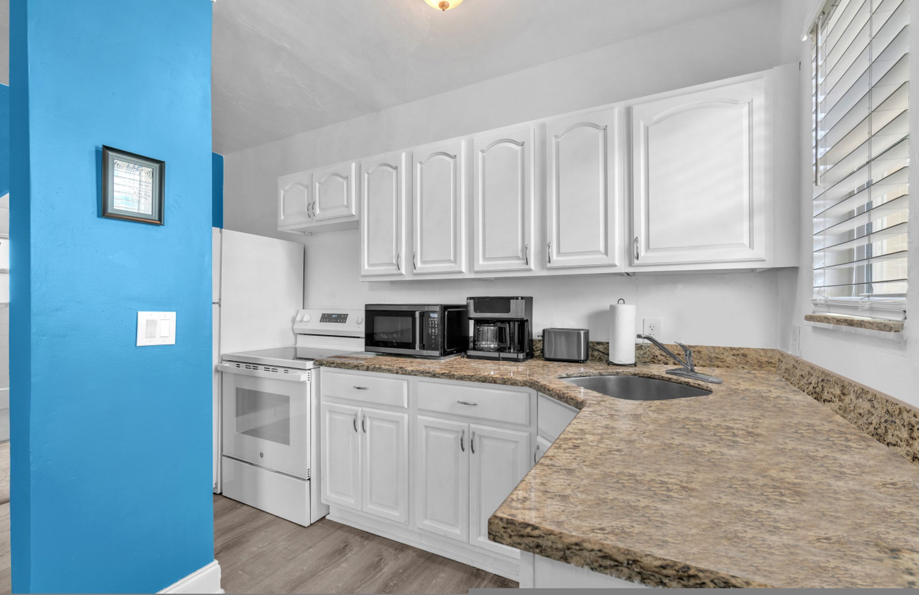 A kitchen with white cabinets, a granite countertop, a microwave, a toaster, and a sink.
