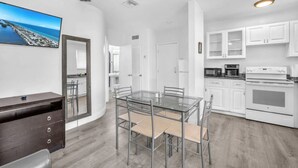 A modern kitchen with white cabinets, a stainless steel oven, and a dining area with a glass table and chairs. - Ultimate Beach Getaway (Hollywood)