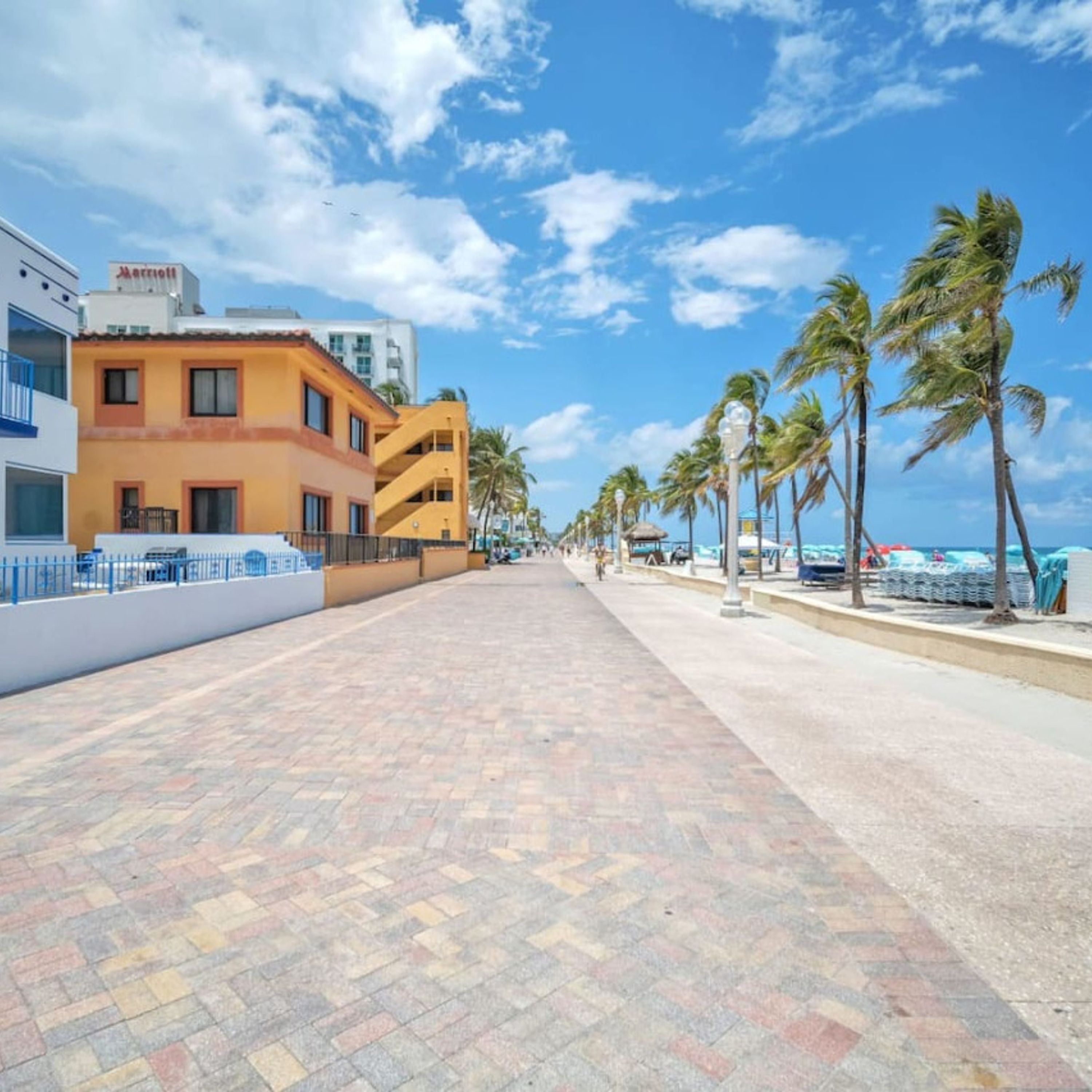 A hotel with a paved walkway, palm trees, and a clear sky.