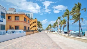 A hotel with a paved walkway, palm trees, and a clear sky. - Ultimate Beach Getaway (Hollywood)