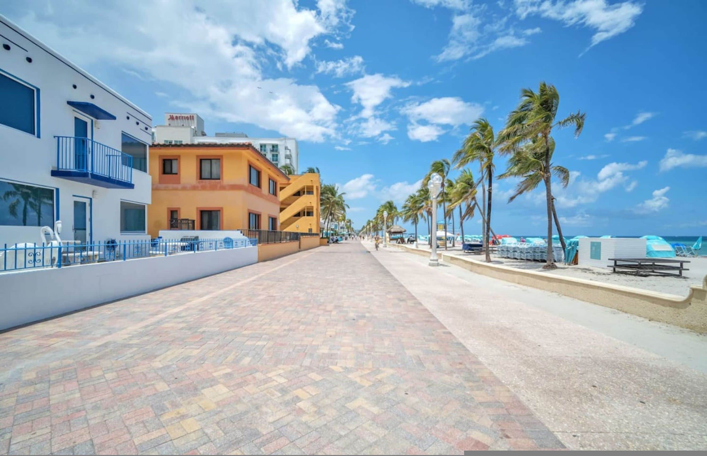 Un hotel con fachada blanca y naranja, un camino pavimentado y palmeras.