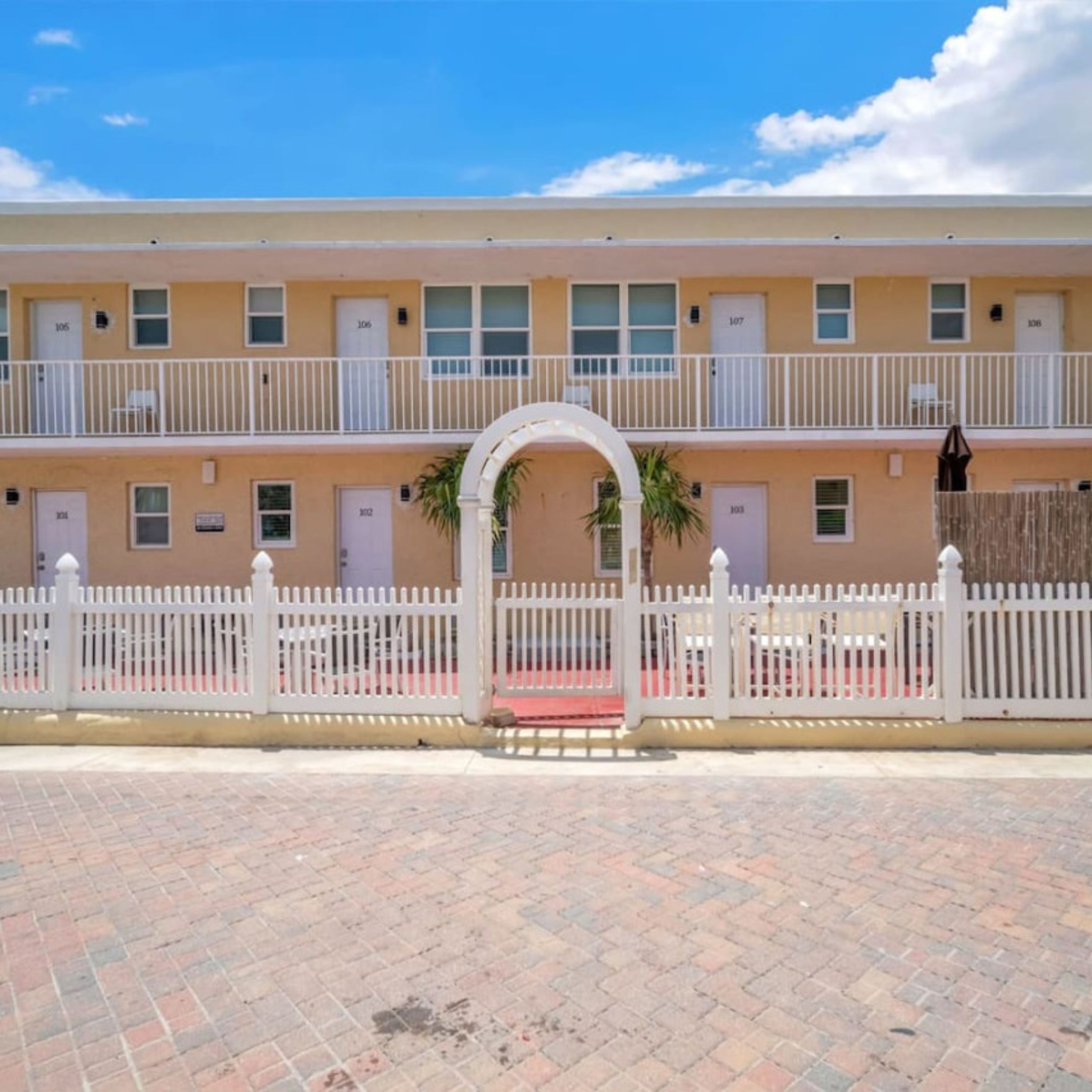 A multi-story building with a white fence, a red bench, and a white archway.