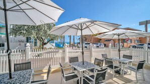 An outdoor patio with white tables and chairs, large umbrellas, and a white picket fence.