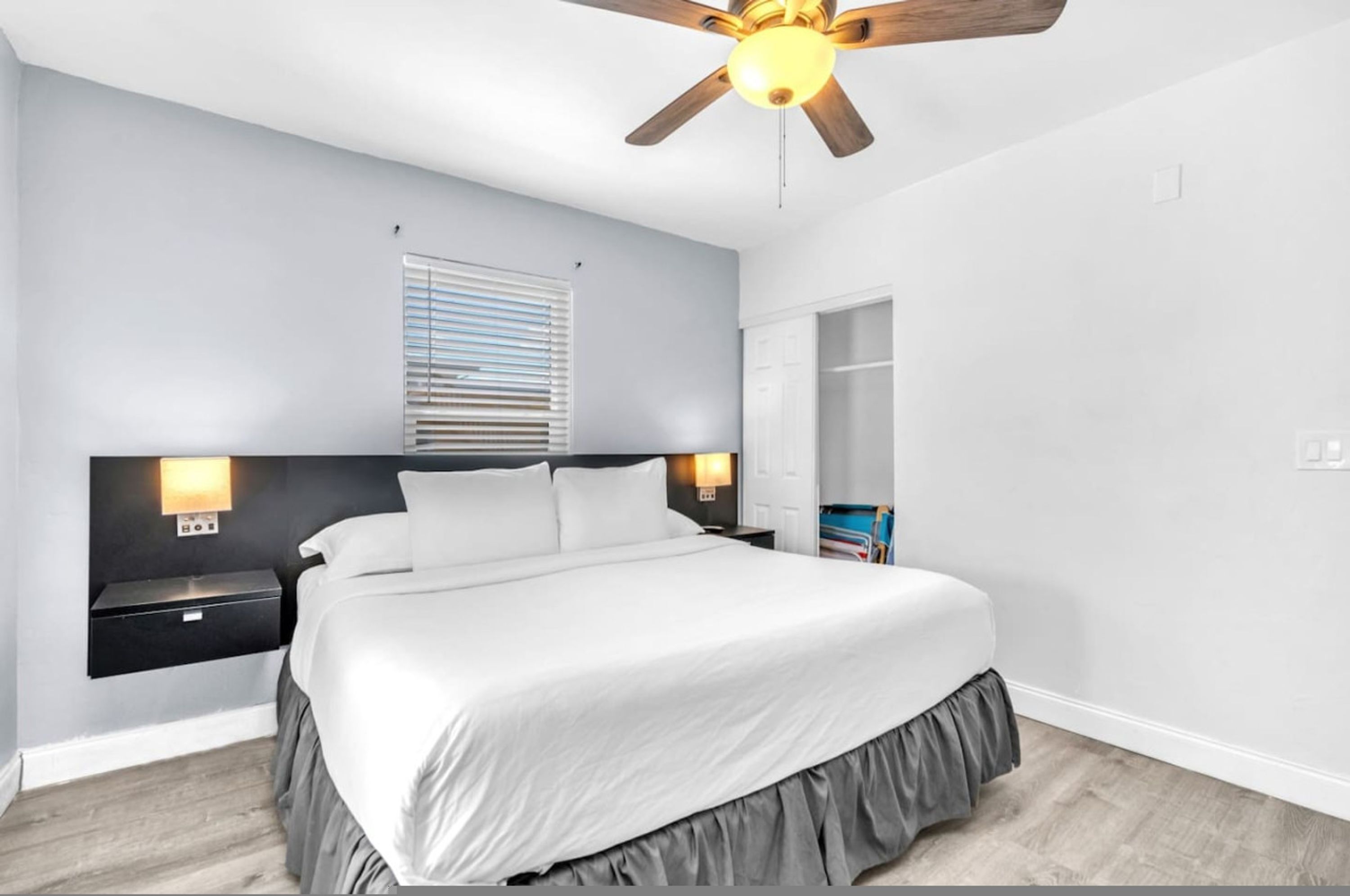 A bedroom with a bed, nightstands, a ceiling fan, a window with blinds, and a built-in wardrobe.
