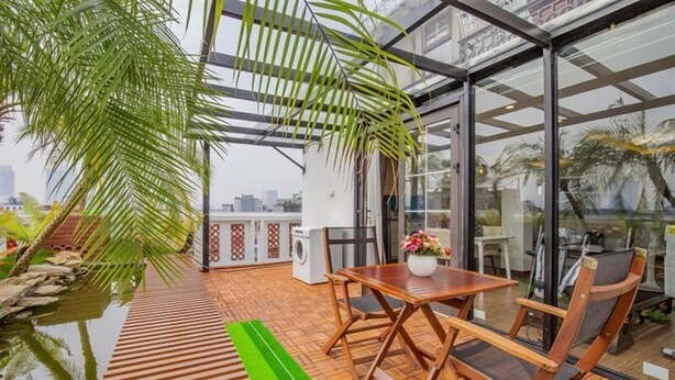 A modern outdoor patio with a wooden table and chairs, a small water feature, and a view of the cityscape through large glass doors. - Sumitomo 2 - 12 Dao Tan (Hanoi)