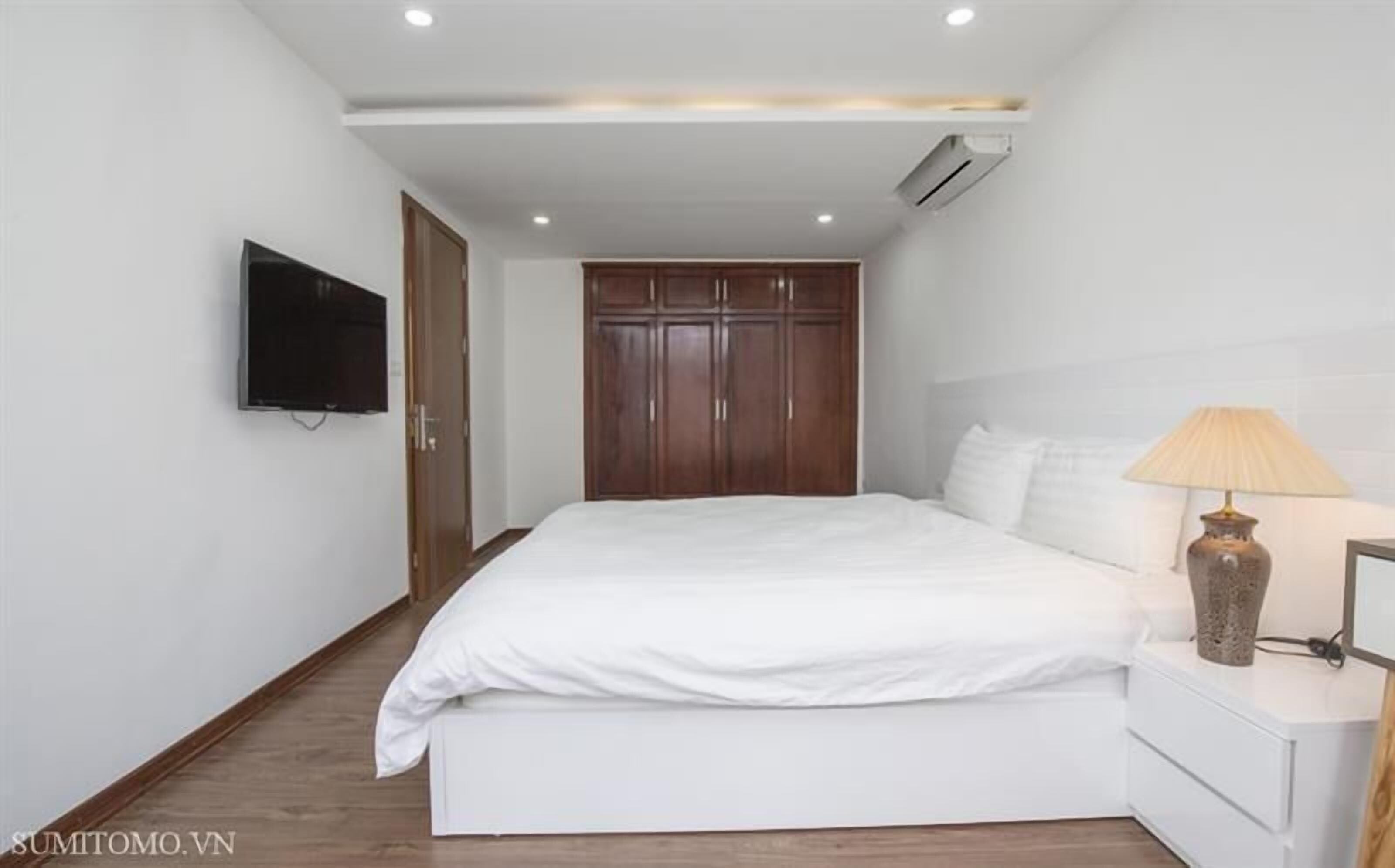 A bedroom with a bed, a nightstand, a lamp, a TV, and a wardrobe.