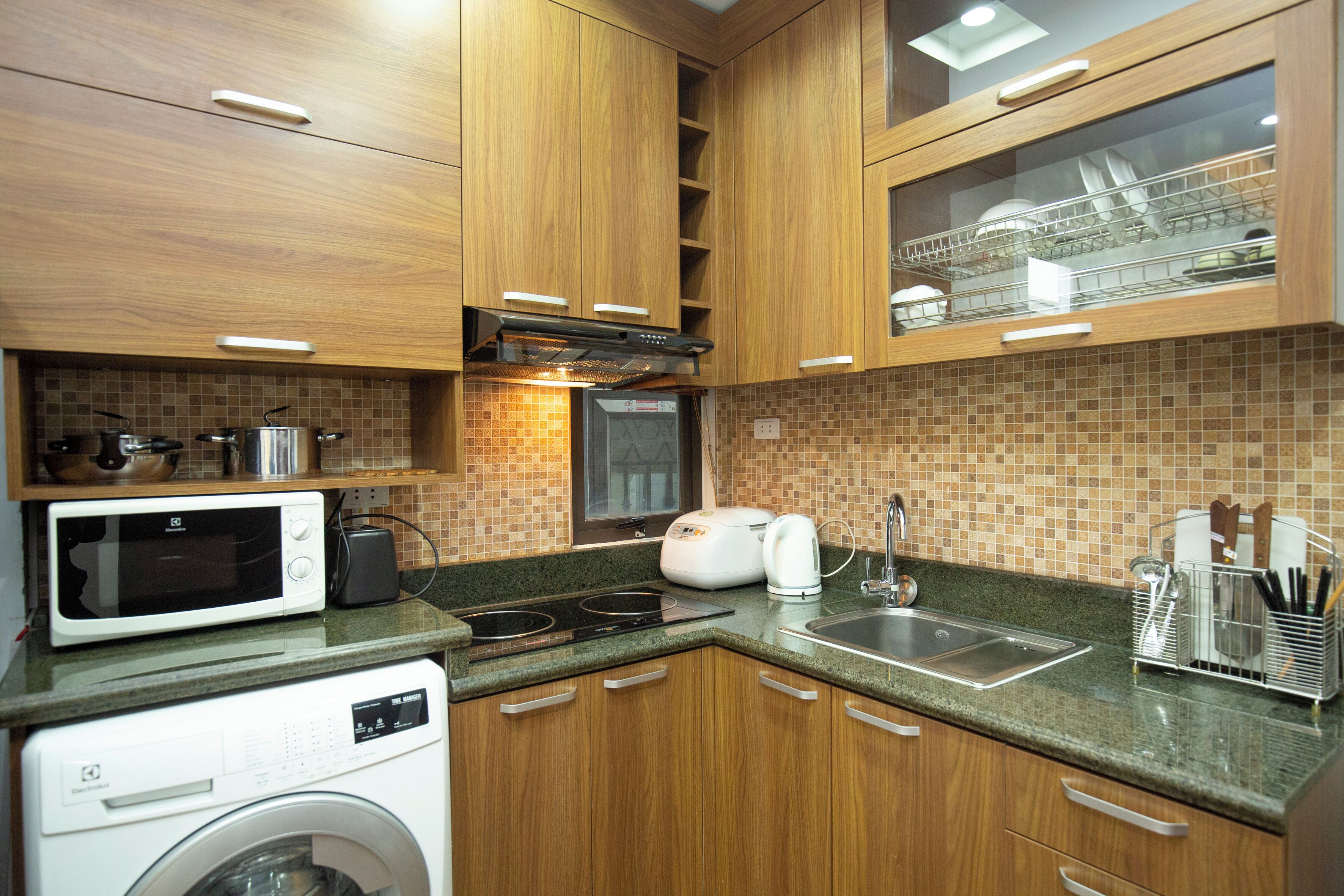 A compact kitchen with wooden cabinets, a microwave, a toaster, a sink, and a dish rack.
