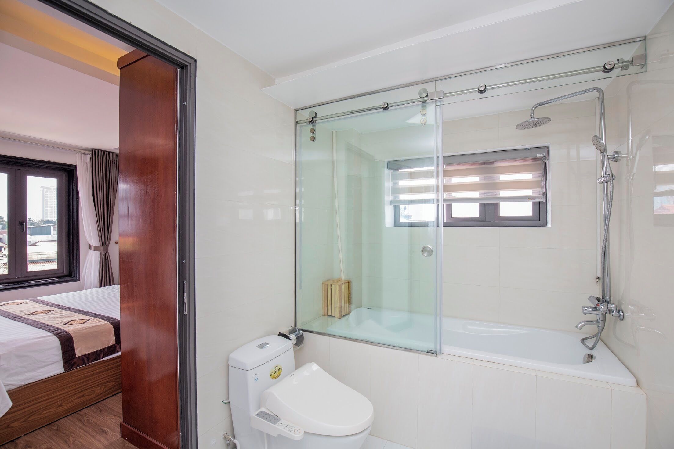 Een moderne badkamer met een glazen douchecabine, toilet en raam.