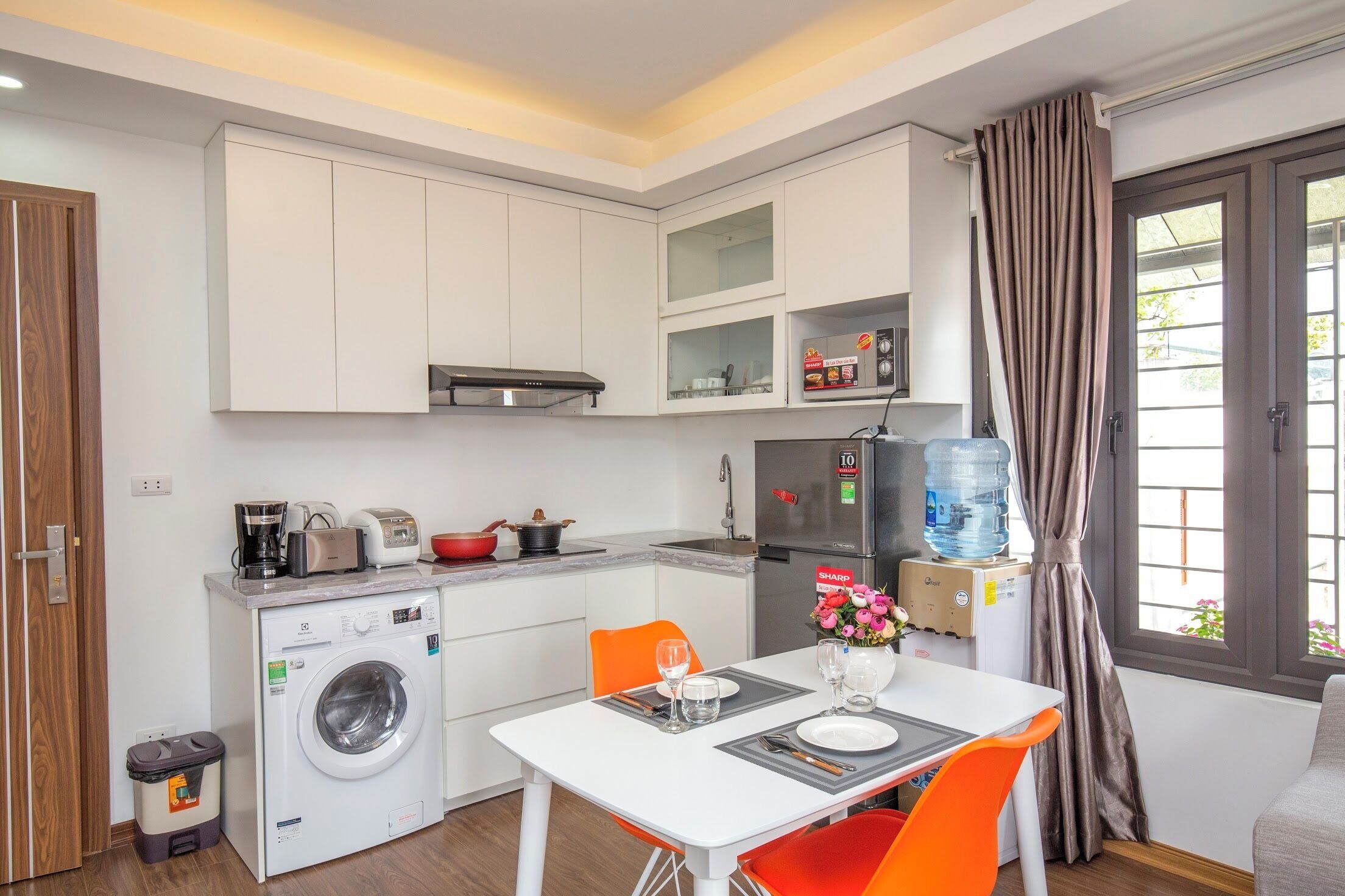 A compact kitchen with a washing machine, a coffee maker, and a water dispenser.