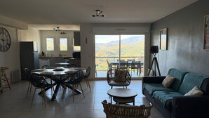 A spacious living area with a dining table, chairs, a sofa, and a balcony with a scenic view.