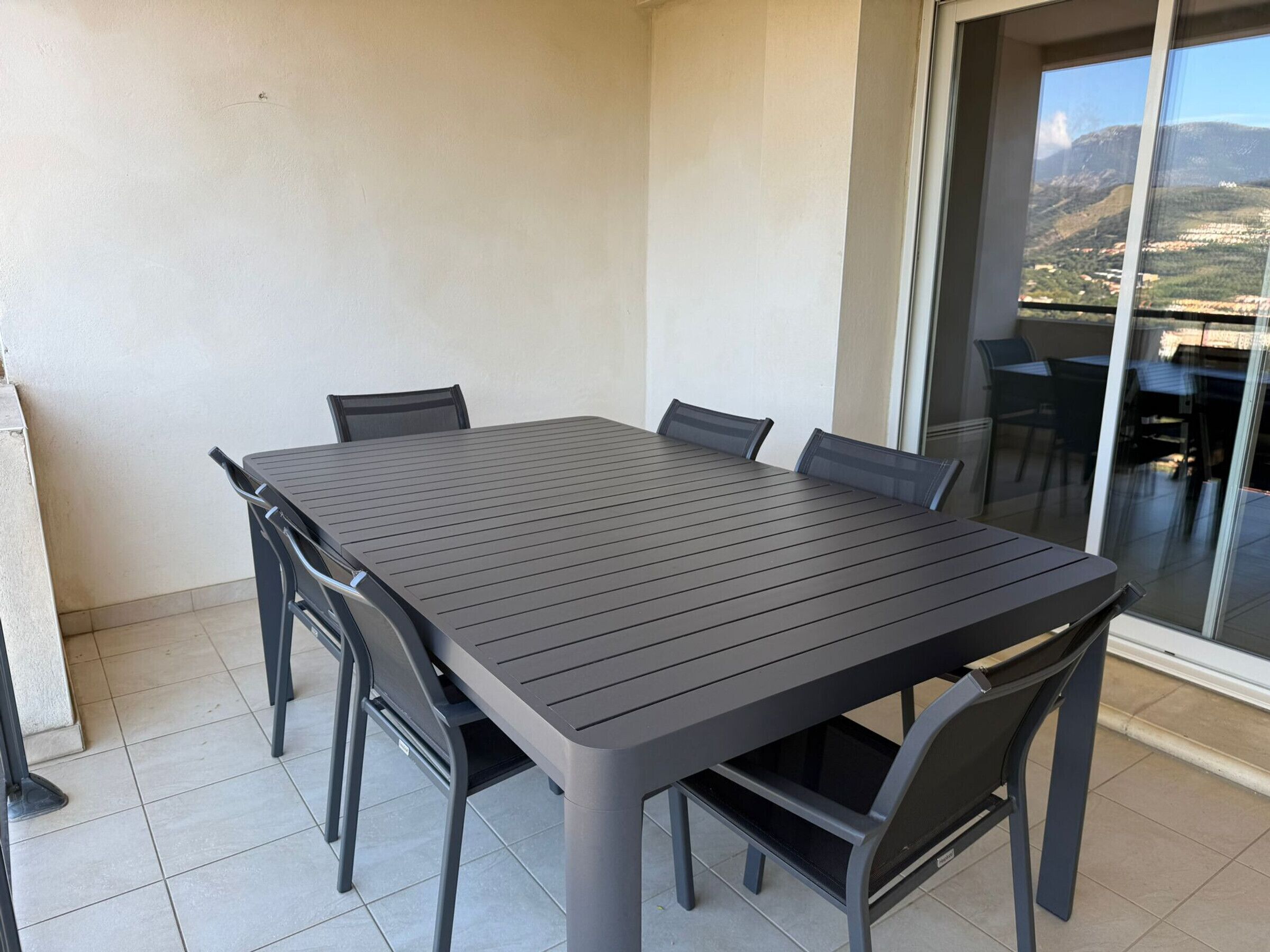 A balcony with a table and chairs, a glass door, and a view of a mountainous landscape.