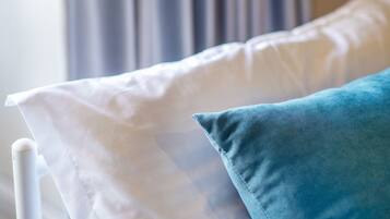 A bed with white and blue pillows, a white headboard, and a window with curtains in the background.