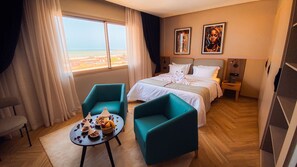 A hotel room with a bed, two chairs, a small table with snacks, a view of the beach, and two paintings on the wall. - Elite View Hotel Dakhla (Dakhla)