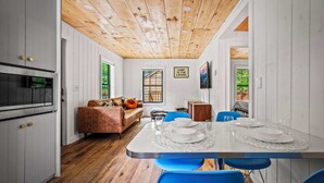 A modern kitchen with white cabinets, a wooden ceiling, and a dining area with a table set for four.