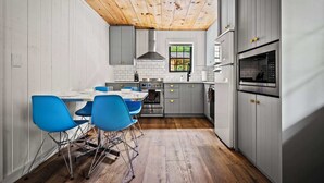 A compact kitchen with white cabinets, a wooden ceiling, and a dining area with blue chairs.