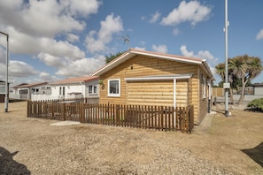 A single-story wooden cabin with a fenced yard, a clear sky, and a palm tree in the background. - Seaside Chalet Retreat in Bridlington (Bridlington)