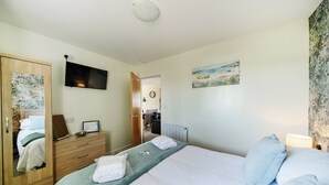 Habitació d'hotel amb llit, armari, televisió, quadre i vista al passadís.