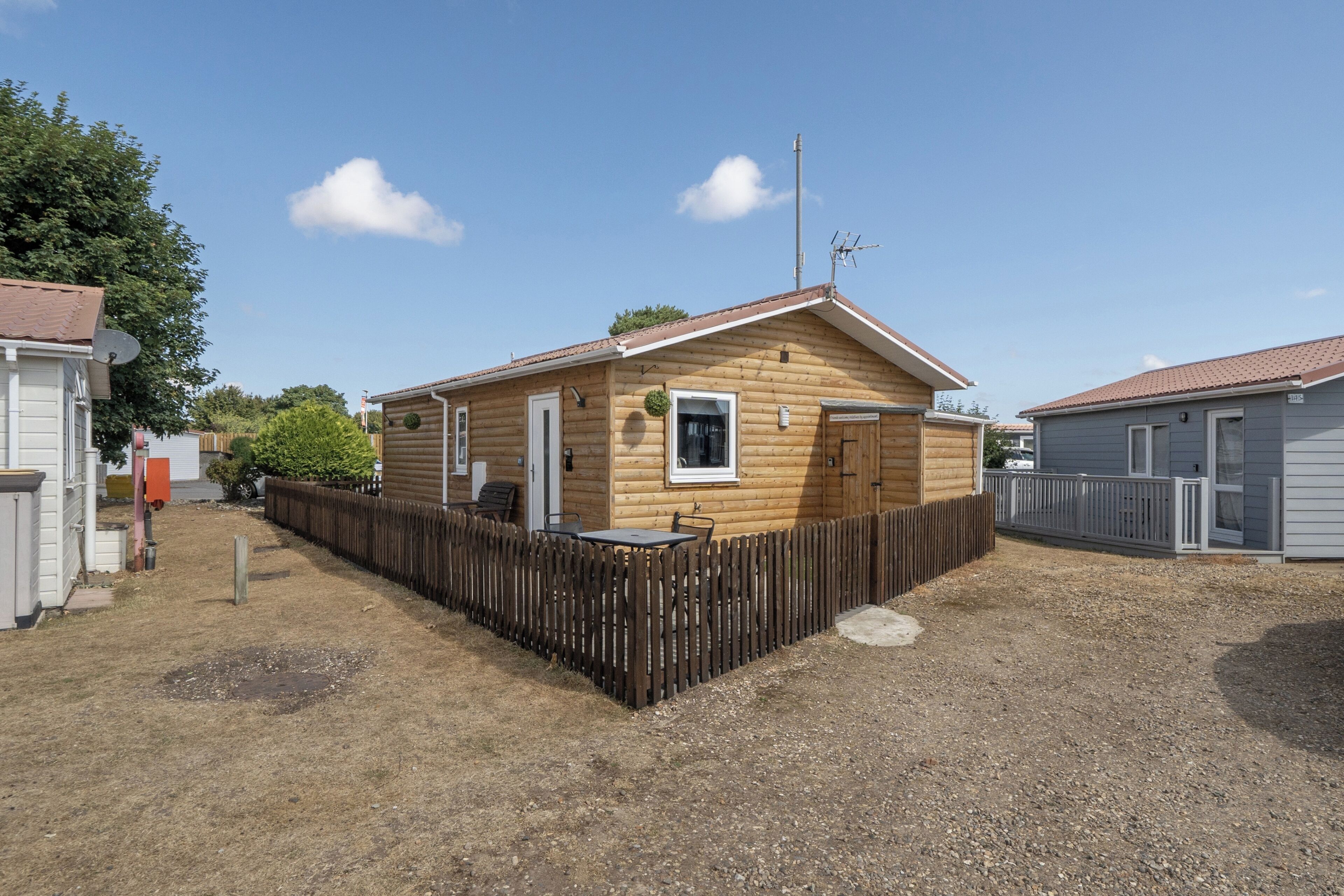 A wooden cabin with a fenced yard, a satellite dish, and a small porch.