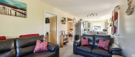 A living room with two black leather sofas, a wooden door leading to a kitchen, and a painting on the wall.