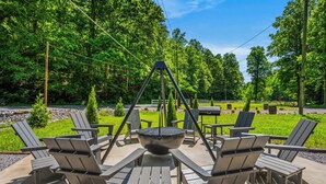 Een buitenruimte met Adirondack-stoelen en een vuurkorf in het midden.