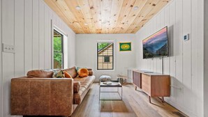 Een moderne woonkamer met een bruine leren bank, een glazen salontafel, een houten kast en een aan de muur bevestigde televisie.