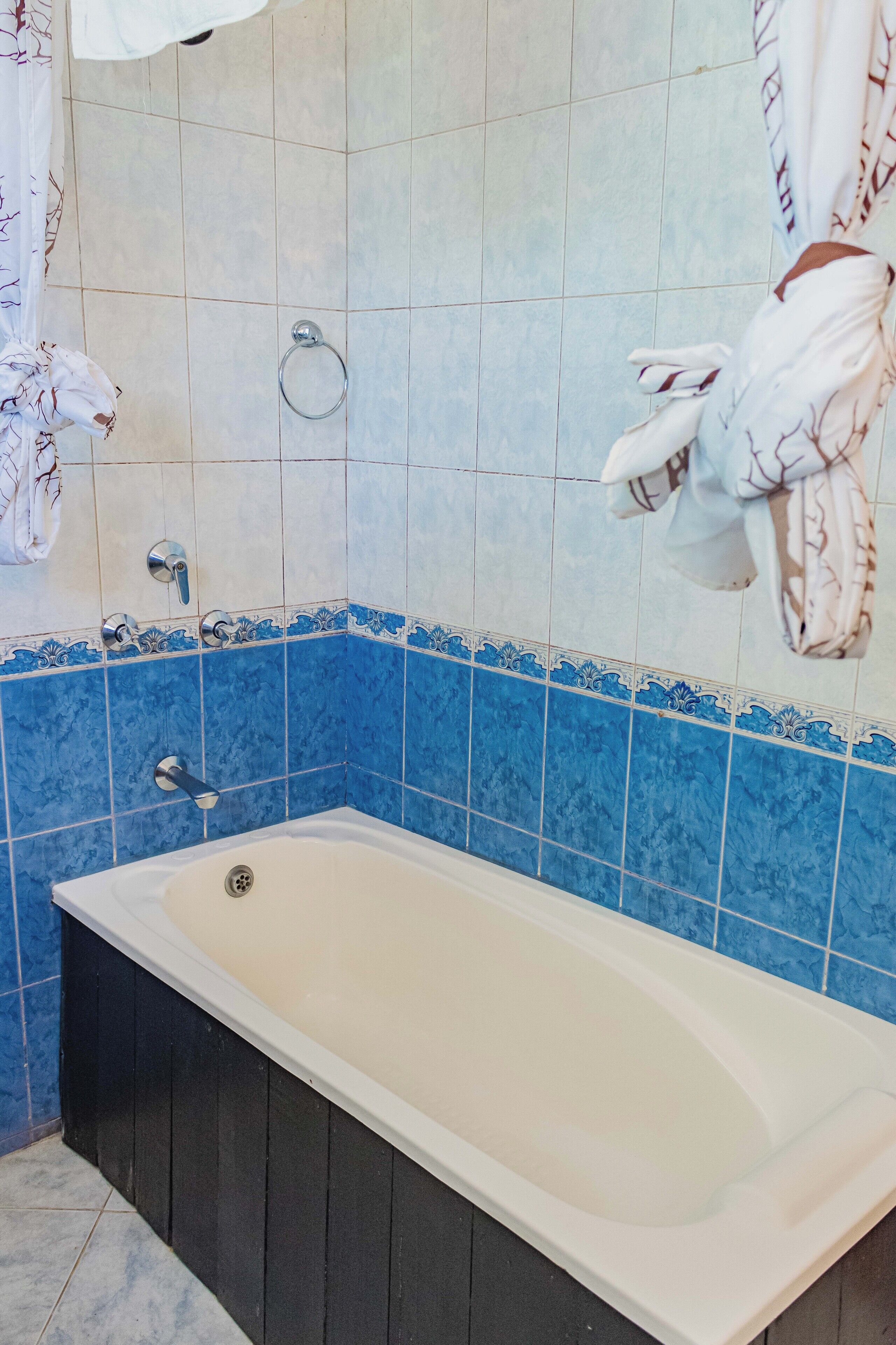 A bathroom with a bathtub, blue and white tiles, a towel ring, and a shower curtain.
