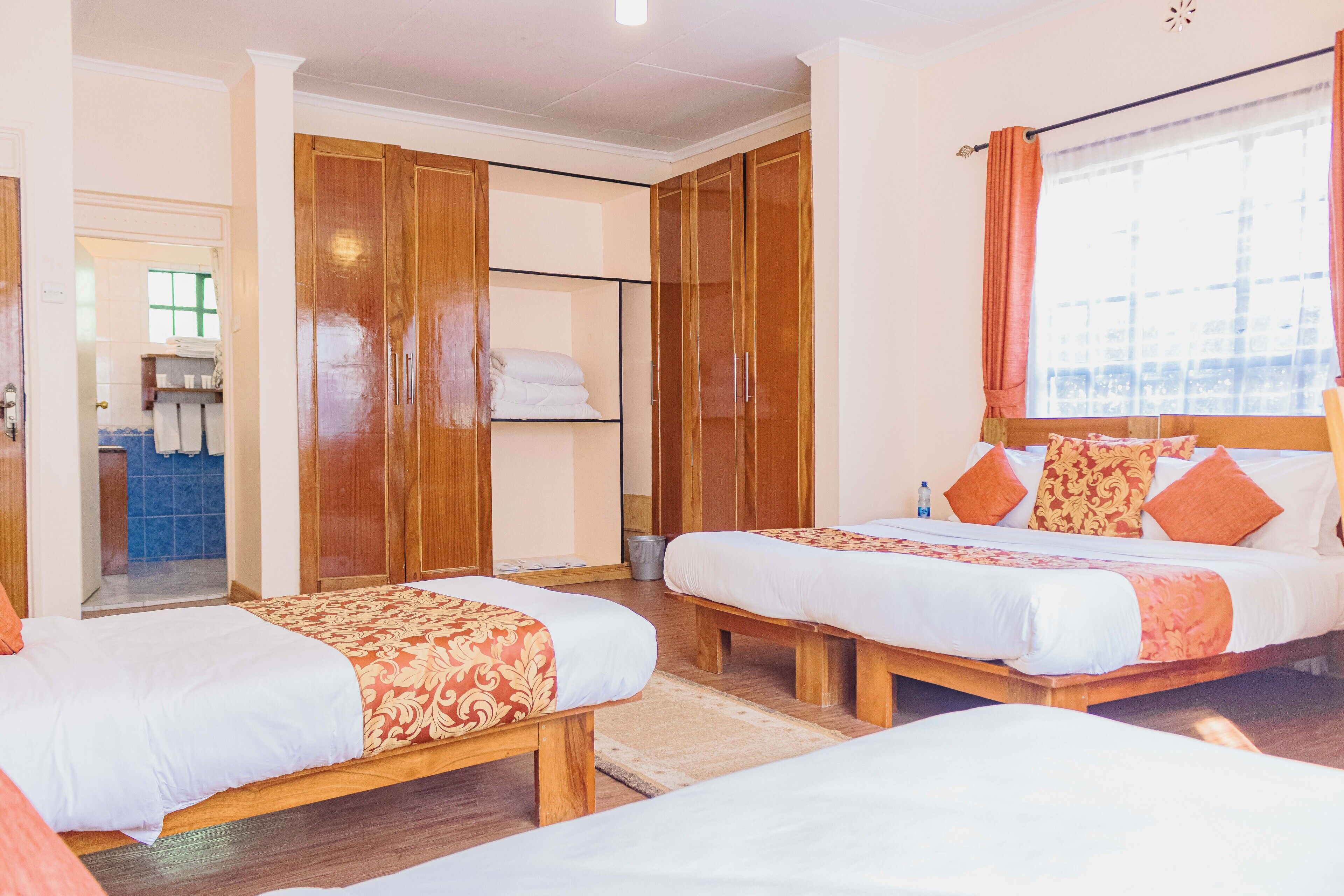 Habitación de hotel con dos camas, armarios de madera, baño con lavamanos y espejo, y ventana con cortinas.