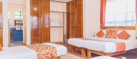 A hotel room with two beds, wooden wardrobes, a bathroom with a sink and mirror, and a window with curtains.