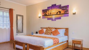 Ein Schlafzimmer mit einem hölzernen Bett, orange-weißer Bettwäsche, einem an der Wand befestigten Spiegel, einem Sonnenuntergangsbild und einem Nachttisch.