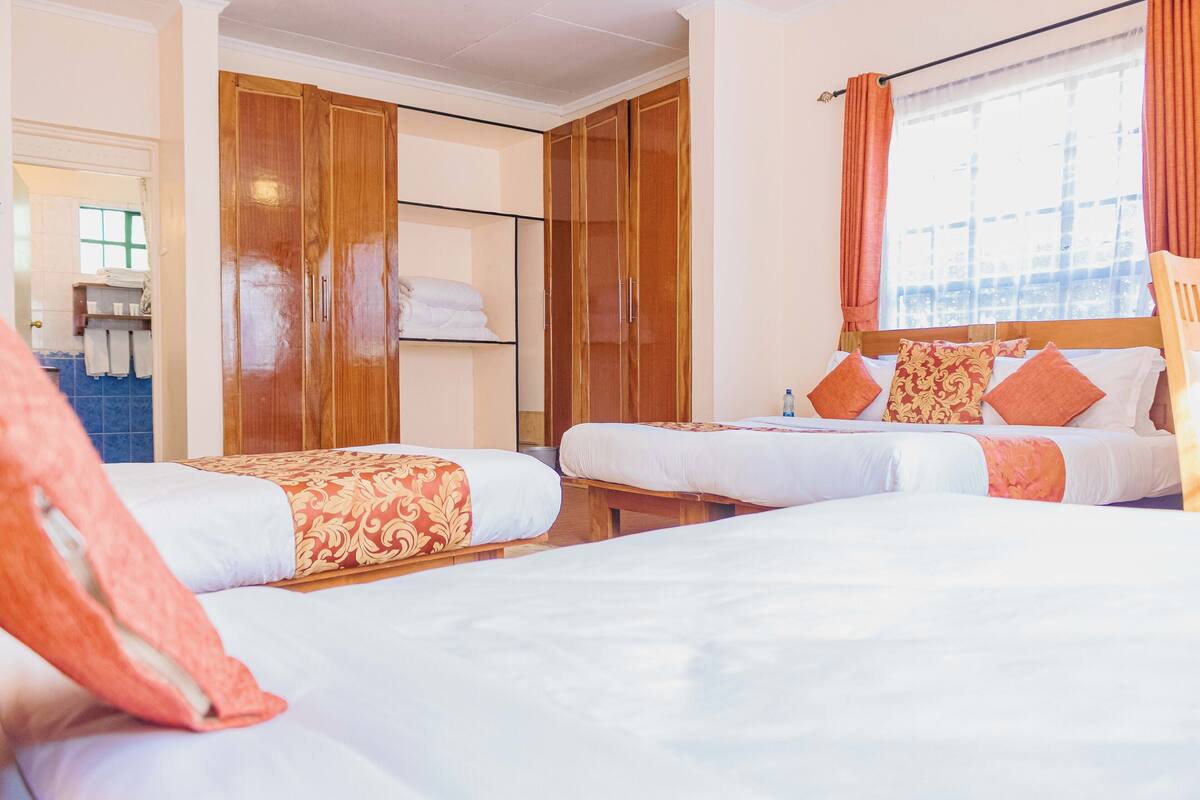 A hotel room with two beds, wooden wardrobes, a bathroom with a blue tiled wall, and a window with curtains.