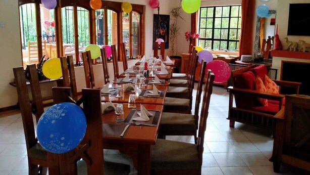 A dining area with long tables set for a meal, wooden chairs, and balloons. - The Farmhouse Inn Nanyuki (Nanyuki)