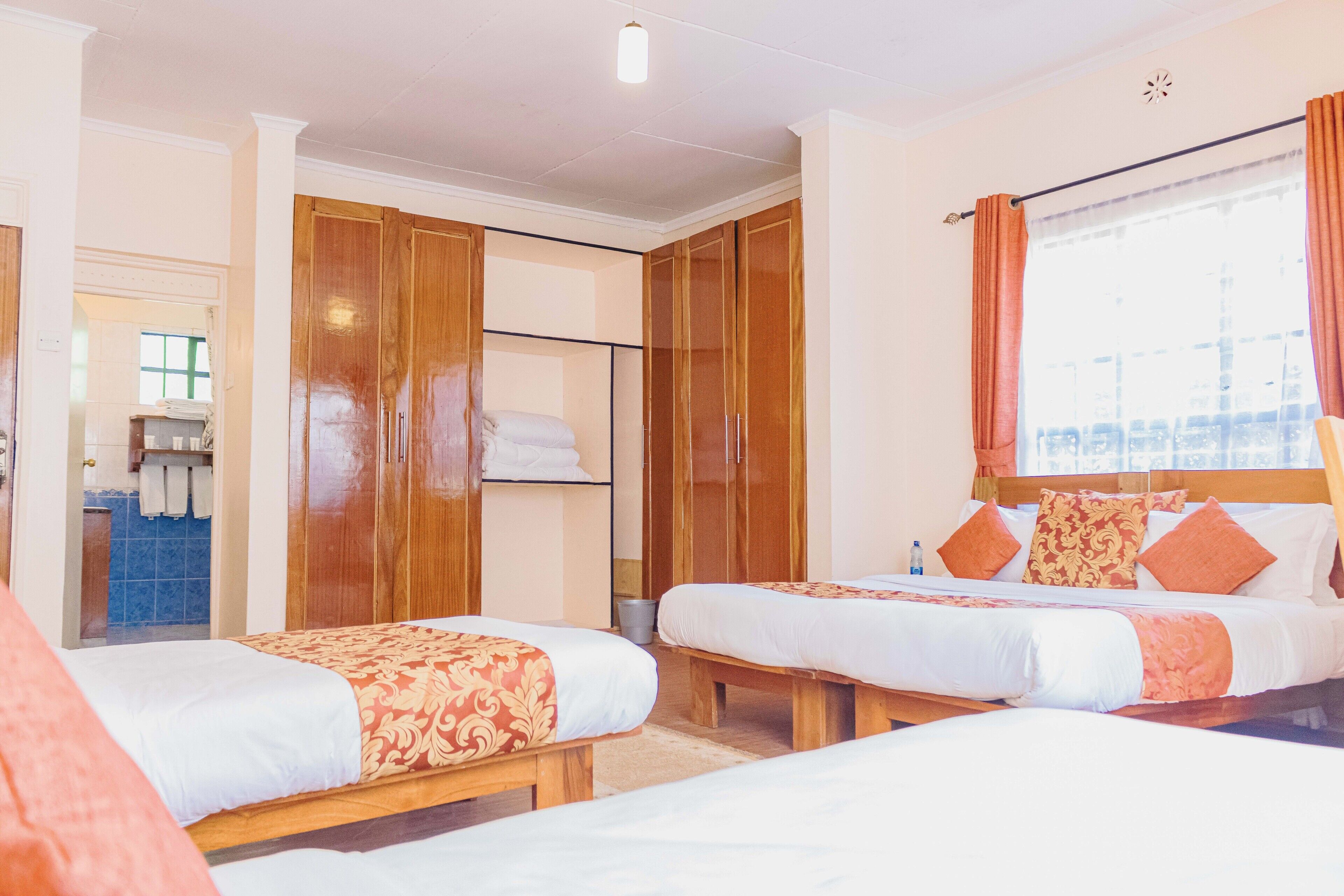Een hotelkamer met twee bedden, houten kasten, een badkamer met blauwe tegels en een raam met gordijnen.
