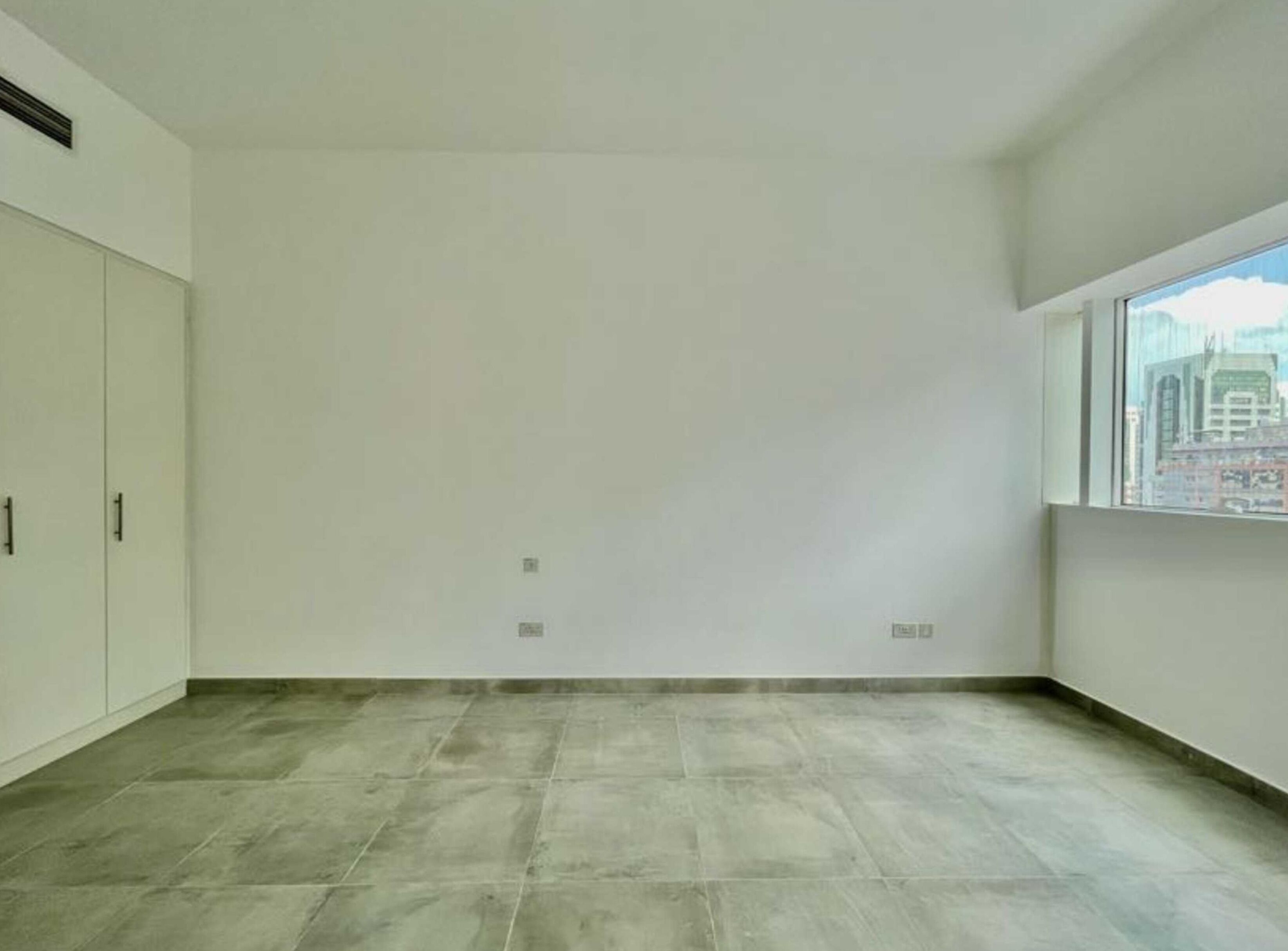 A spacious room with a large window, white walls, and a tiled floor.