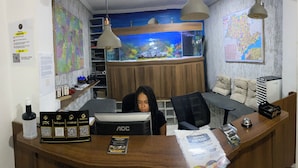 A reception desk with a computer, a map, and a large aquarium in the background. - HOSTEL ANPRADO (Guarulhos)