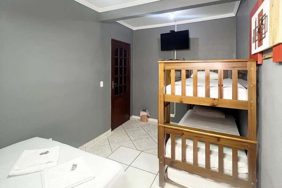 A room with a bunk bed, a ceiling fan, a TV mounted on the wall, and a door.