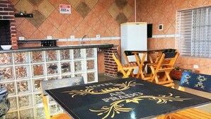 A dining area with a black table and wooden chairs, a brick wall with a tiled backsplash, and a window with blinds. - HOSTEL ANPRADO (Guarulhos)