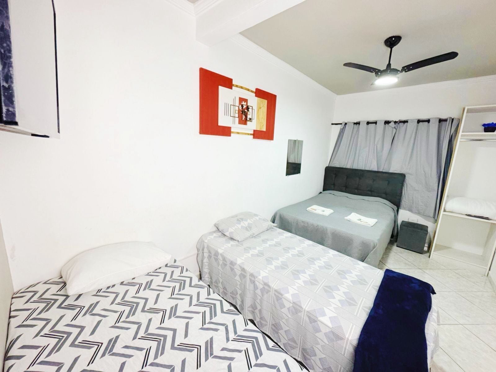 Una habitación con dos camas, ventilador de techo, una obra de arte en la pared y una ventana con cortinas.